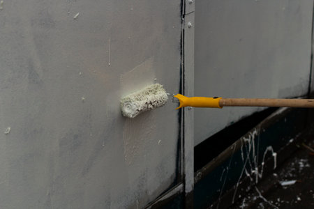 The painter paints with white paint. Paints graffiti with paint. Painting the wall. A worker paints over a vandalist inscription.の写真素材