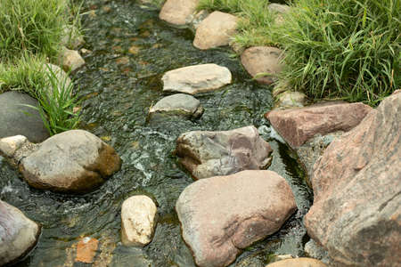 Water runs over the stones. Fresh water stream. Artificial waterfall. Landscaping on the territory.の写真素材