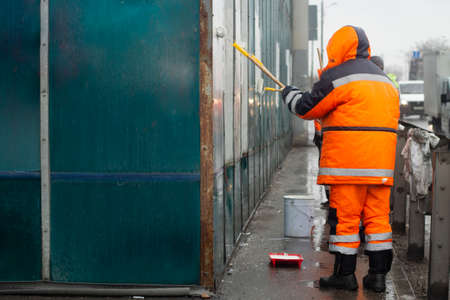 The painter paints with white paint. Paints graffiti with paint. Painting the wall. A worker paints over a vandalist inscription.の写真素材