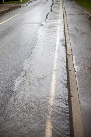 A meadow on a dart. The side of the road is flooded with rain. A lot of water flows along the road.の写真素材