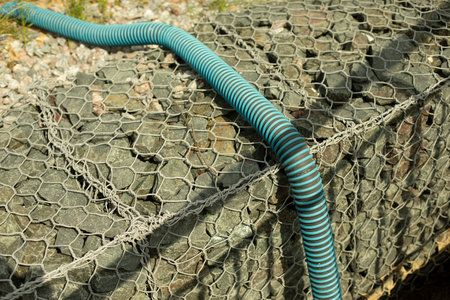 Gaffroned pipe for water supply. A flexible pipe lies on the curb. Stones in a grid.