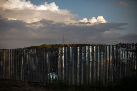 Old fence made of stainless steel. A dented fence outside the city. Sheet metal has fallen into disrepair.の写真素材