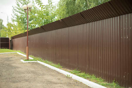 A brown fence encloses the enclosed area. Metal fence along the parking lot. Full protection with a solid fence.の写真素材