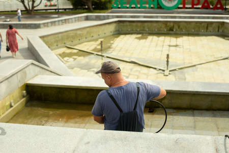 The worker washes the surface from rust. The man washes away the dirt with the help of the pressure of water. City services are cleaning the fountain. The guy is working.の写真素材