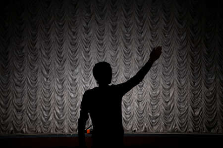 Silhouette of a man in a concert hall. Theater teacher. The man raised his hand up. The beginning of the repitition in the theater. The leader points with an outstretched hand.の写真素材