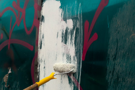 The painter paints with white paint. Paints graffiti with paint. Painting the wall. A worker paints over a vandalist inscription.の写真素材
