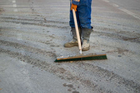 Cleaning the dirt out of the way. A man in boots cleans the surface of the debris. Urgent cleaning on the street. A large mop in the hands of a worker.の写真素材