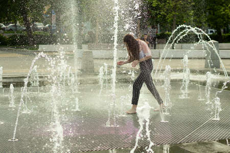 A child runs among the jets of water in the town square. Splashes of the fountain in the summer. A hot day in the city and a source of water.の写真素材