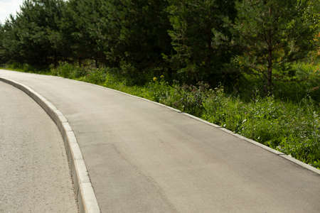 Bend of the road. Rural road with asphalt. Forest along the roadway. Asphalted pedestrian zone. Roads in Russia.の写真素材