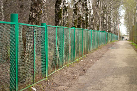 Green fence in kindergarten. An old mesh fence along the road. Fencing school grounds in Russia.の写真素材