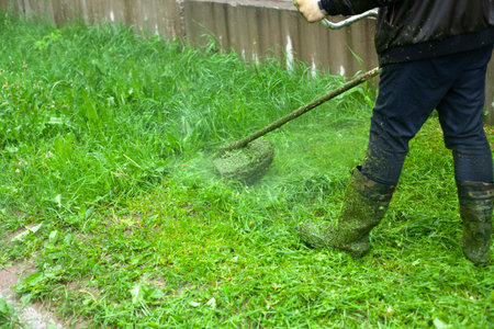 Mows the grass with a hand-held lawn mower. The gardener is cutting the lawn. The gardener's tool cuts tall grass. The lawn mower in action.の写真素材