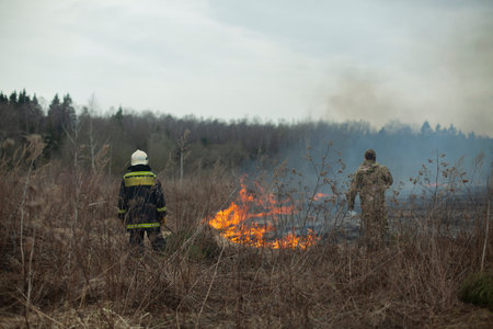 A firefighter extinguishes dry grass. A firefighter is fighting a fire in an open area. Rescuer actions against flames. An ecological catastrophe burns a dry field.の写真素材