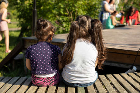 Children sit outside in the summer. Preschoolers in the park. Children sit on a wooden benchの写真素材