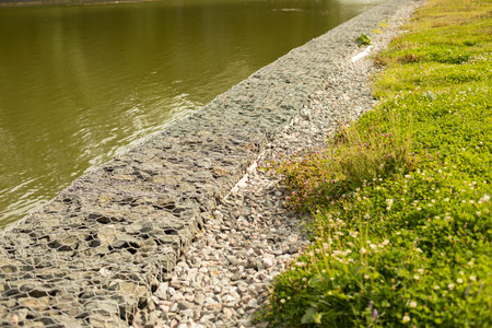 Fortified shore. The shore of the lake is protected from flooding. Stones in a grid hold the coastal part of the pond. The stones are specially laid in a metal mesh.の写真素材