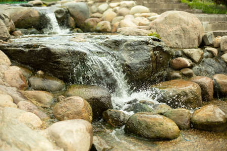 Waterfall among the stones. Artificial pond. Landscape design with stones and water. The flow of water through large cobblestones.の写真素材