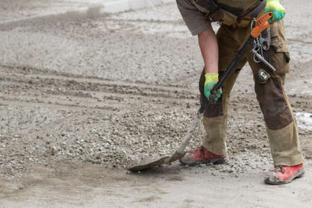 Work with a shovel at a construction site. A worker throws cement and gravel with a shovel. Cleaning the road from scattered building material.の写真素材