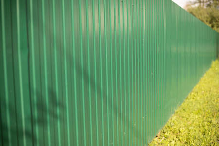 Green fence. Metal fence made of profile sheet. The territory is fenced with a high fence. Ribbed surface on the street. Shooting diagonally.の写真素材