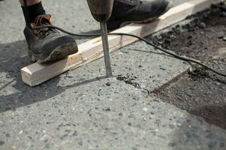 He removes the asphalt with a jackhammer. Removing the asphalt layer from the road. The worker holds a jackhammer. Road repair. Using an electric hammer.の写真素材