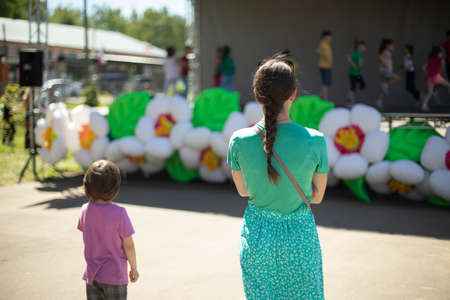 Mother and daughter are watching a performance in the park. Spectators at the event. Street concert for people. Girl with a child in the summer.の写真素材