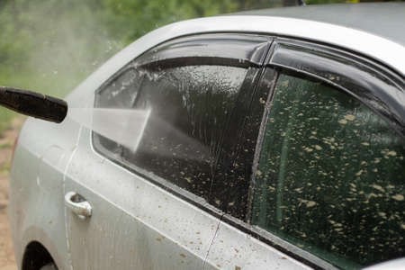 Car wash. The car is washed under the pressure of a jet of water. Using a water spray to wash off dirt from the surface of the car.の写真素材