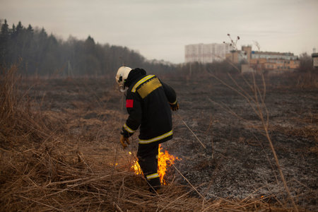 A firefighter extinguishes dry grass. A firefighter is fighting a fire in an open area. Rescuer...