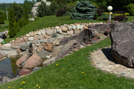 Plants among the stones in the park. Landscaping of the territory. Artificial alpine slide. A place to rest. Garden plants and large cobblestones in the parkland.の写真素材