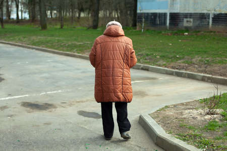 An old woman in Russia. A woman walks down the street in warm clothes. A woman stands on the asphalt. Grandma in town.の写真素材