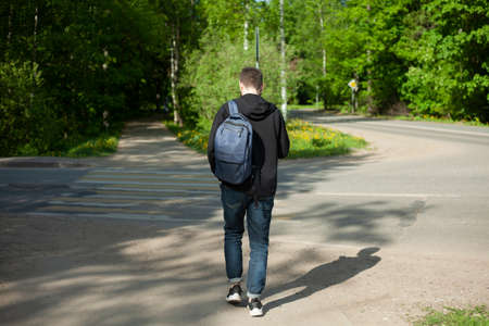 A guy with a backpack walks along the road. The man on the pedestrian road. The man from the back. The man goes to work.の写真素材