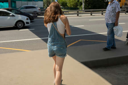 A girl walks along the side of the road in summer. City dweller on the street. The girl from the back.の写真素材