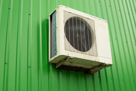 Air conditioning on the wall. Air conditioning outside the store. Green wall made of profiled sheet and white cooling device with fan. Industrial facility in detail.の写真素材