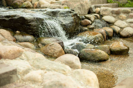 Waterfall among the stones. Artificial pond. Landscape design with stones and water. The flow of water through large cobblestones.の写真素材