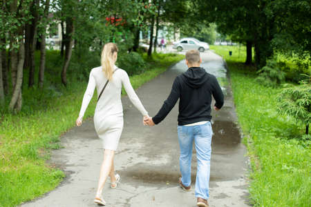 A guy and a girl hold hands. A young couple walks around the city. A couple walk down the street. Young people love each other. Photo from the back.の写真素材
