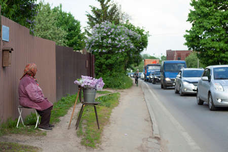 Grandma sells flowers on the road. A pensioner sells lilacs by the side of the road. Poverty in Russia. Flowers from the garden of an old woman.の写真素材