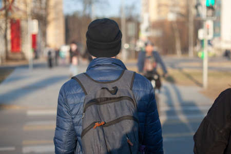 A guy with a backpack from the back. A man with a hat and a backpack. An unknown person walks through the city.の写真素材