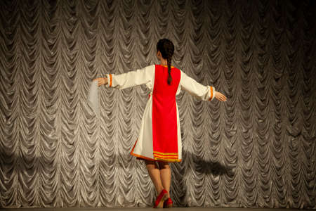 A girl in a folk costume in Russia. Performance on stage. Choreographic lesson. The girl is dancing in a long sundress.の写真素材