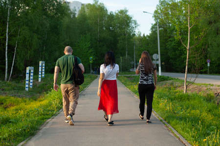 A guy and two girls are walking along the road. Young people are walking down the street. Three people shot from the back. Walk of young people around the city.の写真素材