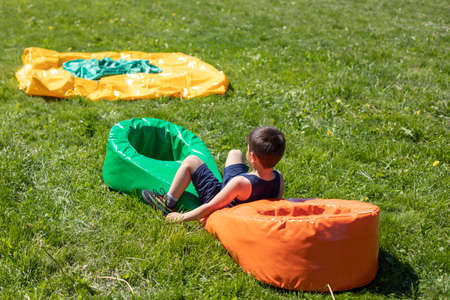 The baby's playing in the yard. Children's summer holidays. A sports obstacle for a preschooler. The boy jumps over a soft poof on the lawn.の写真素材