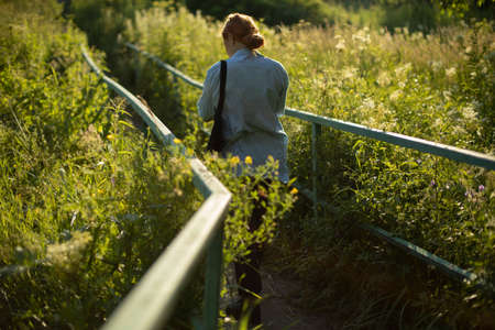 The girl walks alone in the park. A girl walks among the thickets in the summer. The schoolgirl returns on a deserted road.の写真素材