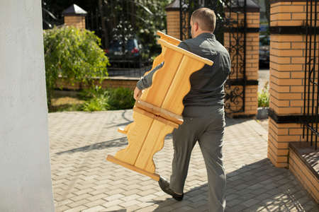 The guy carries two wooden benches. The man is dragging objects. Preparation of the event. An employee drags furniture in the summer.の写真素材