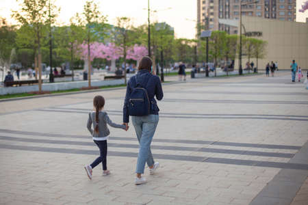 Mom and daughter are holding a hand. A woman walks with a child across the square. Family walk. People rush home.の写真素材