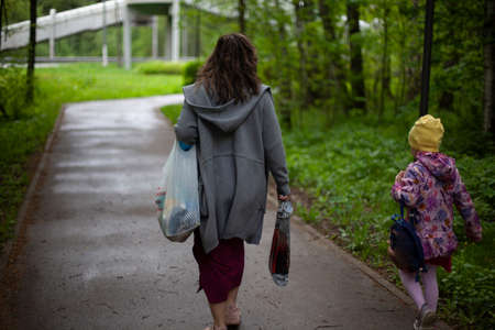 Mom and daughter are walking in the park. The woman and daughter are in a hurry to get to work. Walk to the bus. People from the back.の写真素材