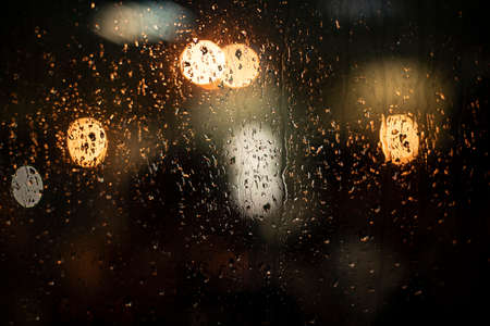 Raindrops on the glass. Blurry background with lights. The texture of the glass on a dark background. Blurred lights of round shape.の写真素材
