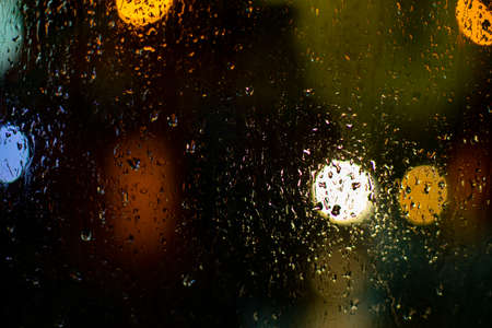 Raindrops on the glass. Blurry background with lights. The texture of the glass on a dark background. Blurred lights of round shape.の写真素材