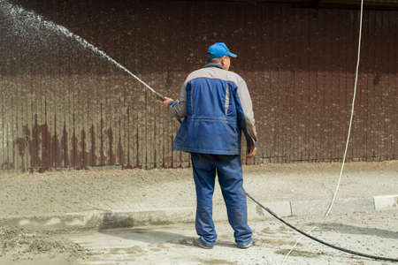 A man washes the fence with a hose. The builder cleans the fence from dirt. Cleaning at a construction site.の写真素材