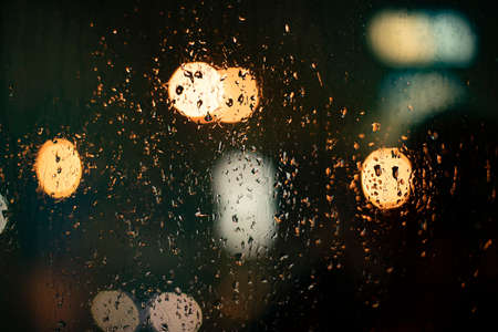 Raindrops on the glass. Blurry background with lights. The texture of the glass on a dark background. Blurred lights of round shape.の写真素材