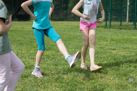 Children are dancing on the lawn. The girls are filming and dancing. Jumping girls on a hot day. Children are having fun. Shooting without faces.の写真素材