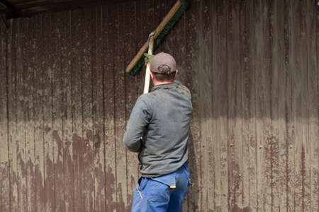 Cleans the fence with a mop. A worker washes the fence from the mud. The guy after construction work cleans the fence of stuck cement. The man works hard.の写真素材