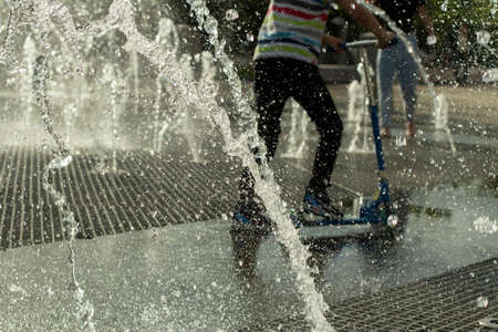 Children run among the jets of water. Droplets of liquid fly in the air. Rest of children in summer in the park.の写真素材