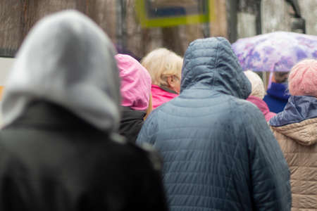 People from the back in the rain. Hooded people walk towards the bus. It's raining outside. Bad weather for people.の写真素材