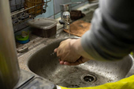 Hand washing in the sink. The bachelor washes his fingers with soap. Dirty sink in the house. Water pours from the tap.の写真素材